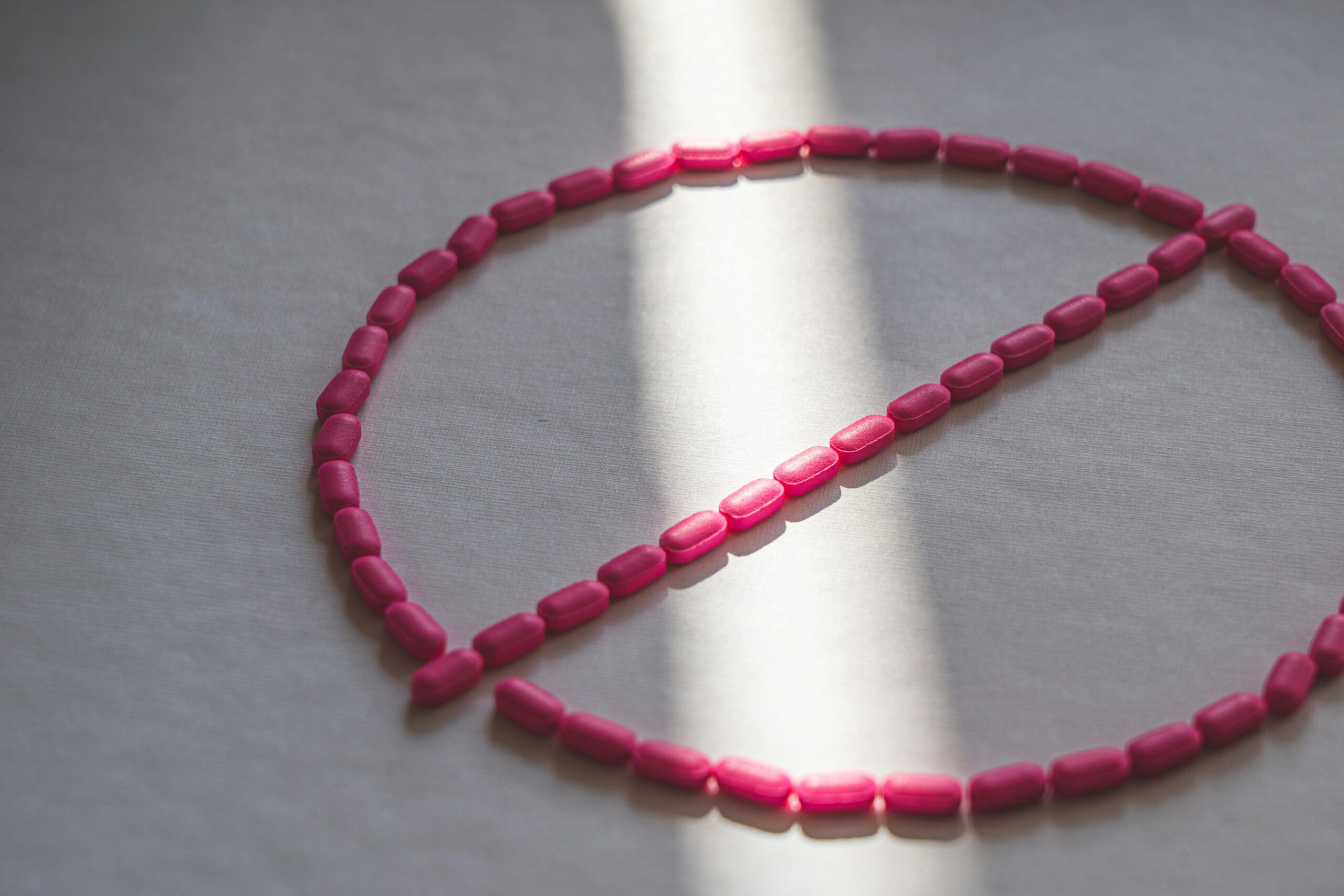 Pink pills arranged in a no-entry symbol under sunlight, symbolizing prohibition.